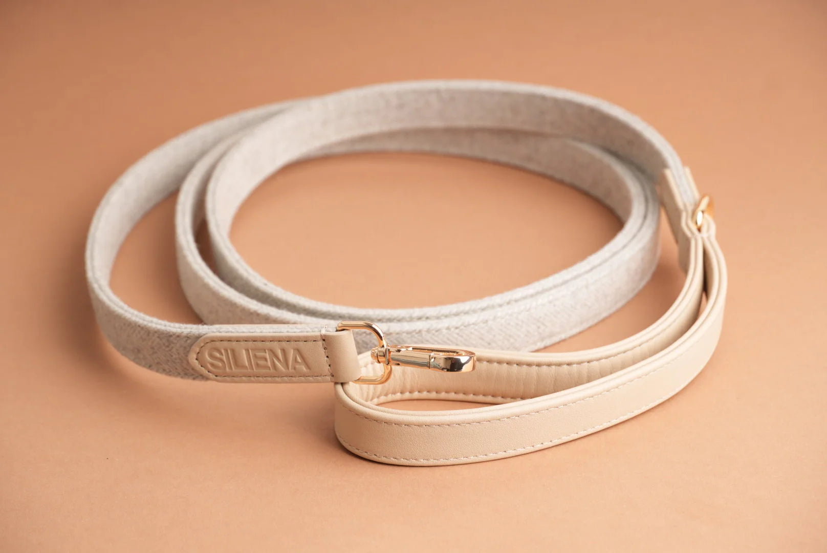 Helle Hundeleine aus Textil mit Echtleder-Details und goldfarbenem Karabiner von Siliena auf beigefarbenem Hintergrund.