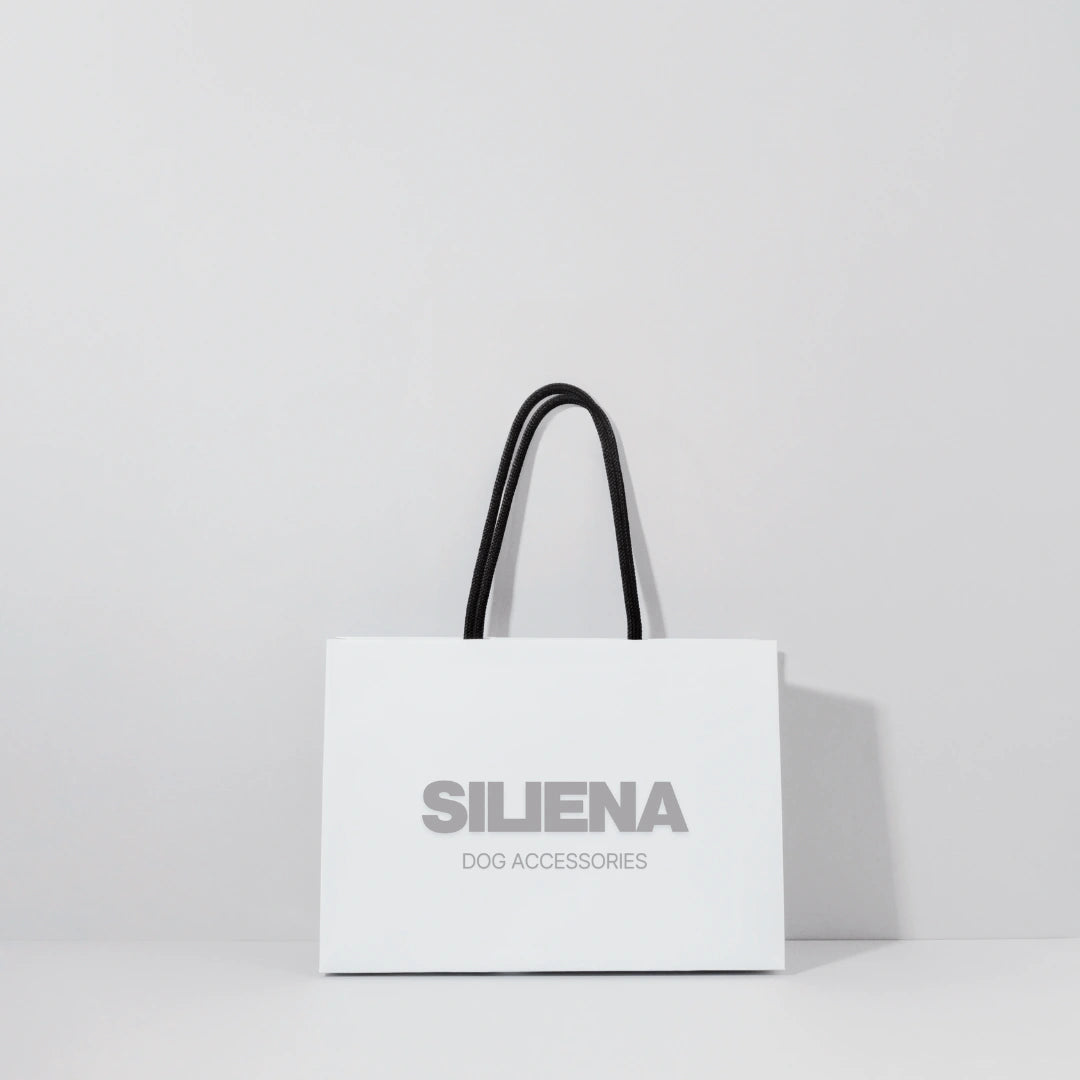 Weiße Einkaufstasche mit Siliena Dog Accessories Logo und schwarzen Henkeln vor hellgrauem Hintergrund